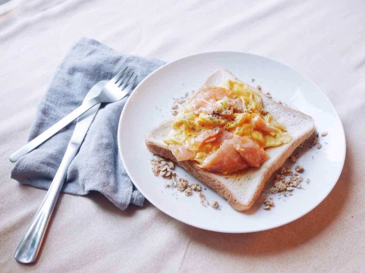 Sandwich mit Rührei und Lachs auf einem hellen Teller